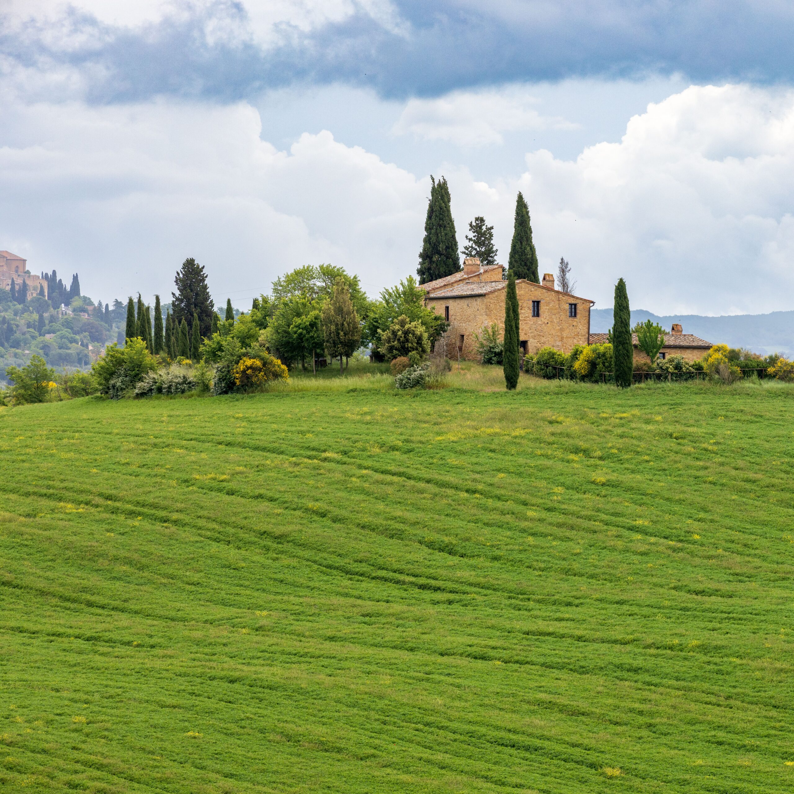 Peaceful view of a rustic house amid rolling hills and cypress trees in Tuscany, Italy.